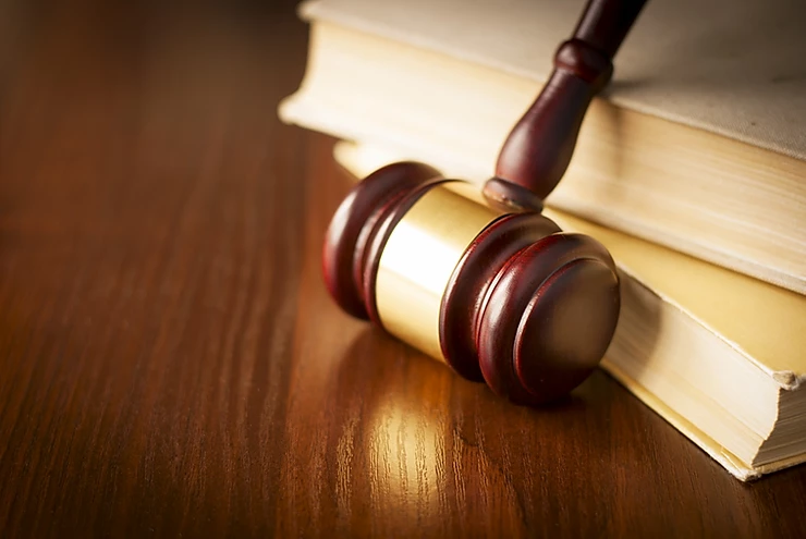 A wooden gavel rests on top of a closed legal book on a polished wooden surface, symbolizing law and justice.