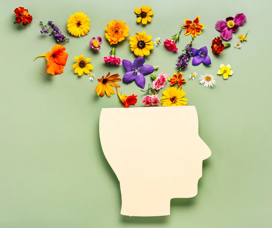 A paper cutout of a human head on a green background with colorful flowers arranged to look like they are blooming out of the head, symbolizing creativity or imagination.