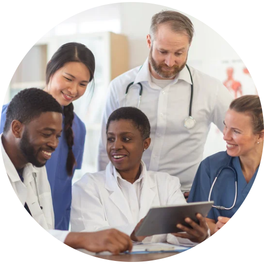 Five healthcare professionals, including doctors and nurses, are gathered around a table. One holds a tablet, and they are smiling and discussing something together. Medical equipment and charts are visible in the background.
